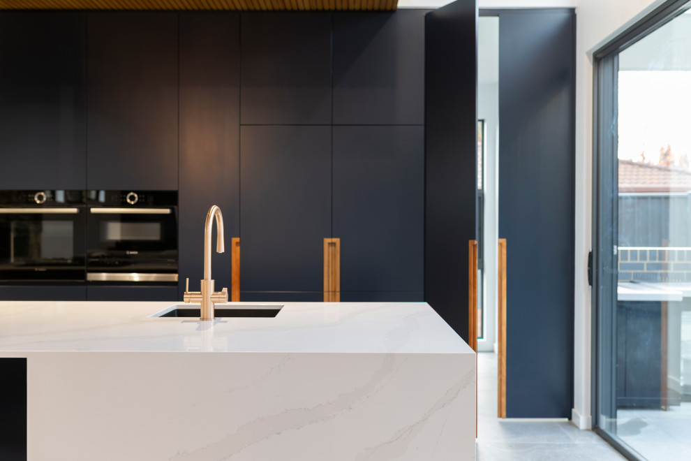 Photo of a large modern galley open plan kitchen in Canberra - Queanbeyan with an undermount sink, blue cabinets, quartz benchtops, black appliances, porcelain floors, with island, grey floor and white benchtop.