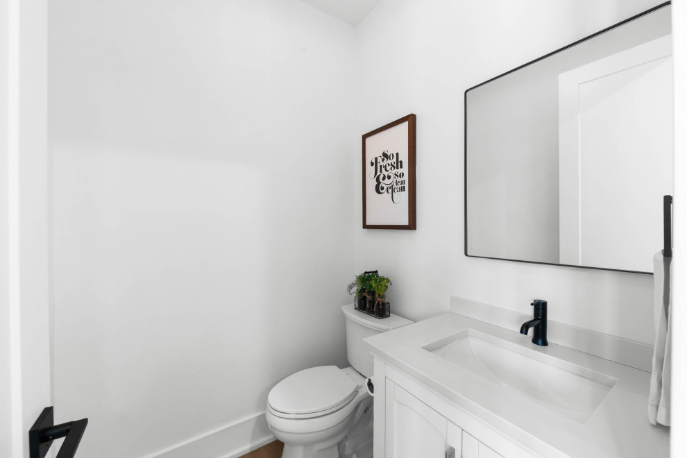 Design ideas for a mid-sized country powder room in Nashville with beaded inset cabinets, white cabinets, a one-piece toilet, white walls, medium hardwood floors, a drop-in sink, engineered quartz benchtops, white benchtops and a built-in vanity.