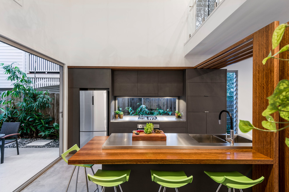 This is an example of a modern galley open plan kitchen in Brisbane with flat-panel cabinets, grey cabinets, stainless steel benchtops, stainless steel appliances, concrete floors, with island, grey floor, an integrated sink and window splashback.