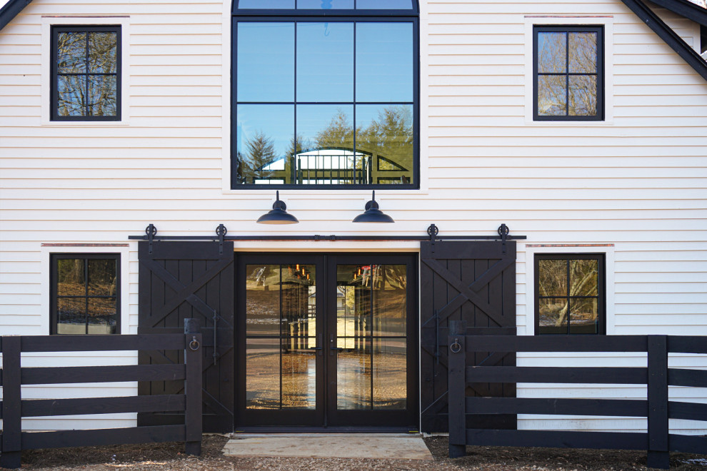This is an example of a mid-sized country front door in DC Metro with white walls, medium hardwood floors, a double front door, a black front door, brown floor, exposed beam and planked wall panelling.