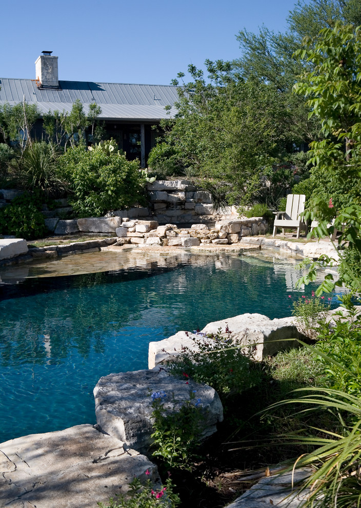 Mid-sized country backyard custom-shaped natural pool in Austin with natural stone pavers and a hot tub.
