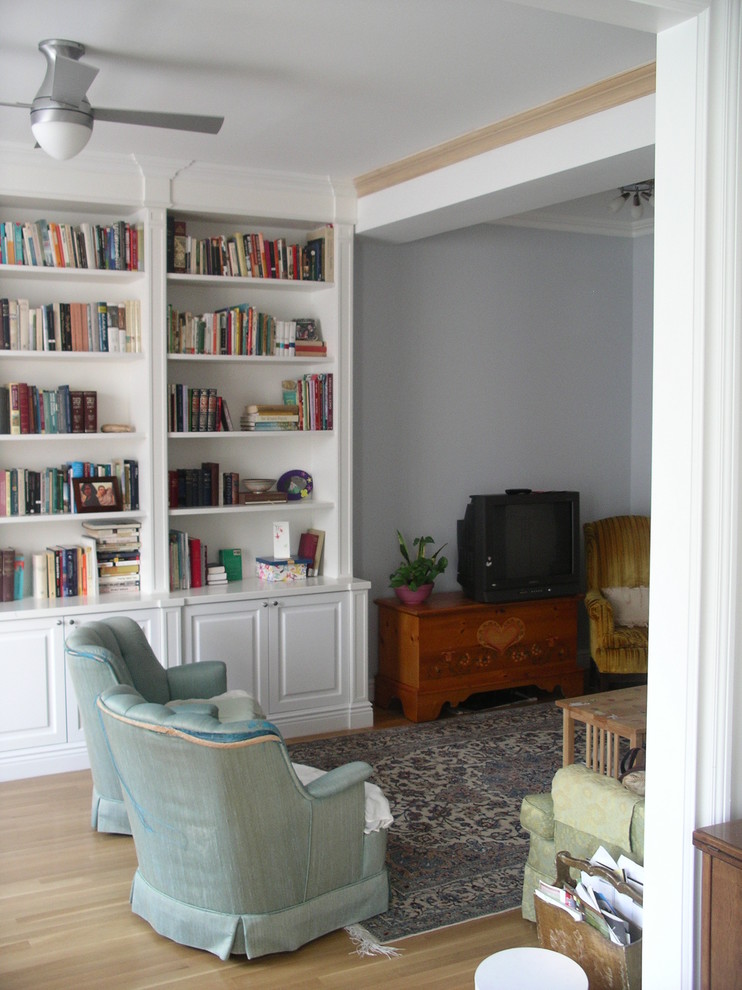 Mid-sized transitional home office in New York with a library, grey walls, light hardwood floors, a standard fireplace and a plaster fireplace surround.