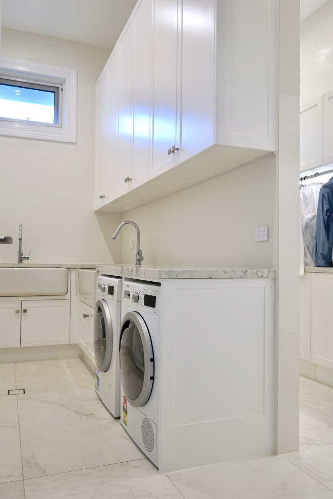 Large modern u-shaped dedicated laundry room in Sydney with a farmhouse sink, shaker cabinets, white cabinets, quartz benchtops, white splashback, porcelain splashback, white walls, marble floors, a side-by-side washer and dryer, white floor and white benchtop.