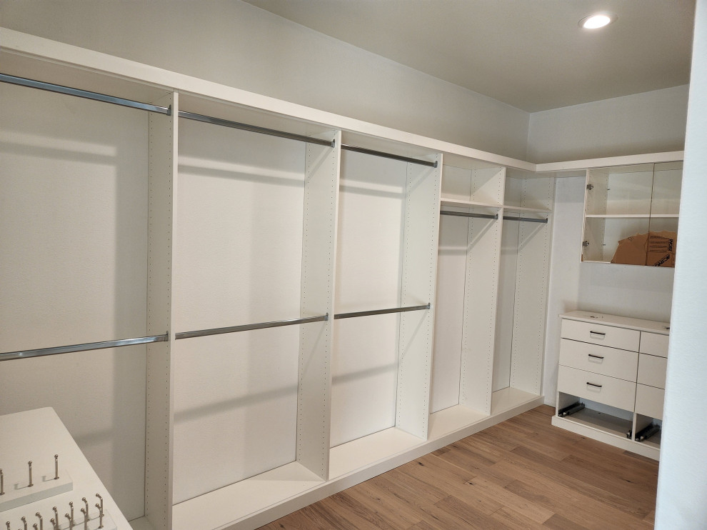 Foto de armario vestidor grande con armarios con paneles lisos, puertas de armario blancas y suelo de madera clara