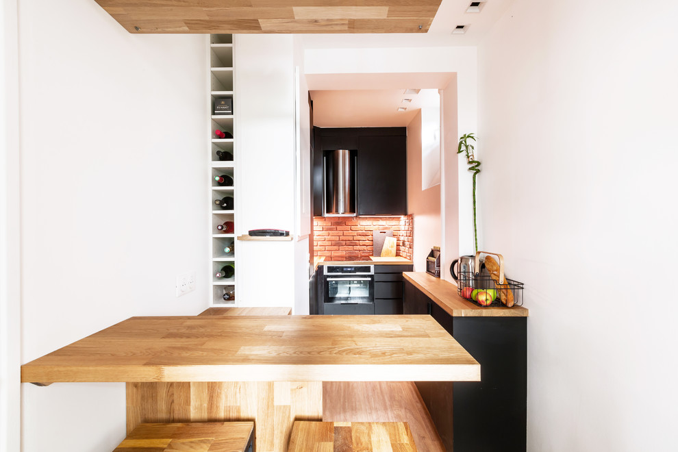 Photo of a mid-sized u-shaped open plan kitchen in Paris with an undermount sink, beaded inset cabinets, black cabinets, wood benchtops, orange splashback, matchstick tile splashback, stainless steel appliances, medium hardwood floors, multiple islands, brown floor and brown benchtop.