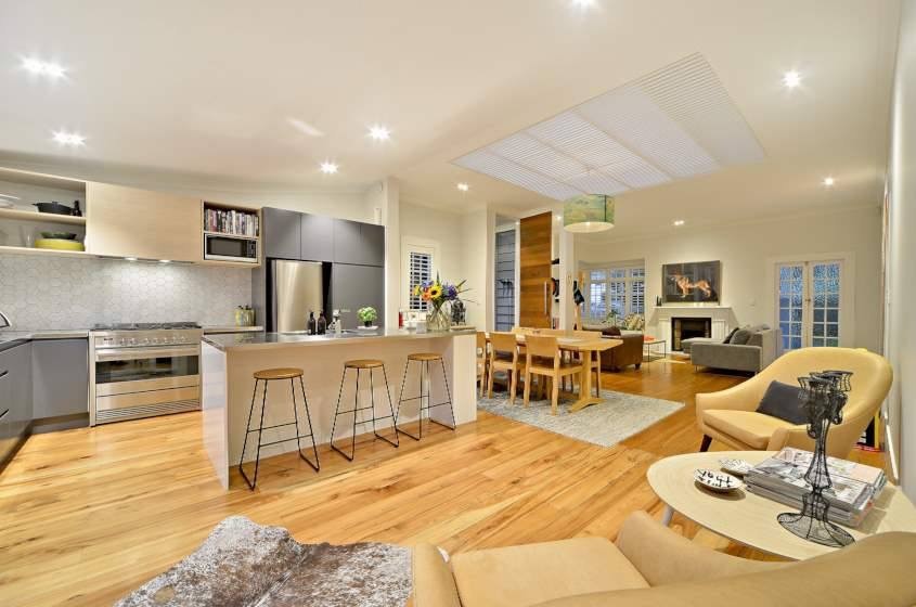 This is an example of a mid-sized beach style l-shaped eat-in kitchen in Auckland with a double-bowl sink, stainless steel benchtops, ceramic splashback, stainless steel appliances, light hardwood floors, with island and yellow floor.
