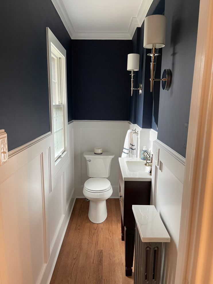Cette photo montre un petit WC et toilettes chic en bois foncé avec un placard à porte shaker, WC séparés, un mur bleu, un sol en bois brun, un lavabo encastré, un plan de toilette en quartz modifié, un sol marron, un plan de toilette blanc, meuble-lavabo sur pied et boiseries.