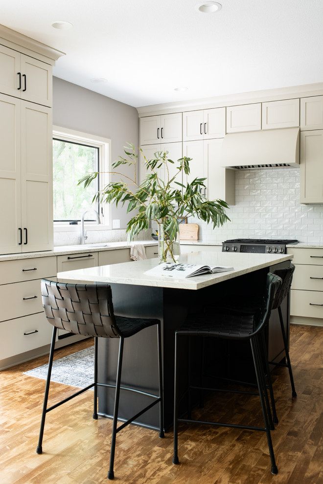 Mid-sized transitional u-shaped medium tone wood floor and brown floor eat-in kitchen photo with an undermount sink, shaker cabinets, white cabinets, quartz countertops, white backsplash, subway tile backsplash, black appliances, an island and white countertops