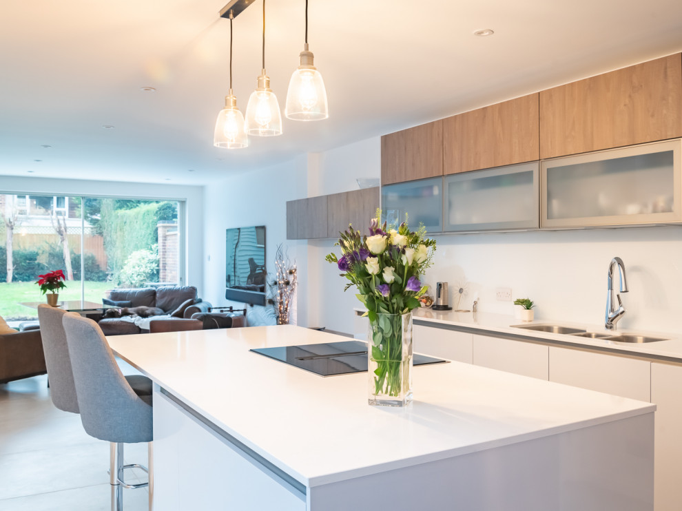 This is an example of a mid-sized contemporary galley eat-in kitchen in Berkshire with a triple-bowl sink, flat-panel cabinets, grey cabinets, quartzite benchtops, white splashback, glass sheet splashback, black appliances, porcelain floors, with island and white benchtop.