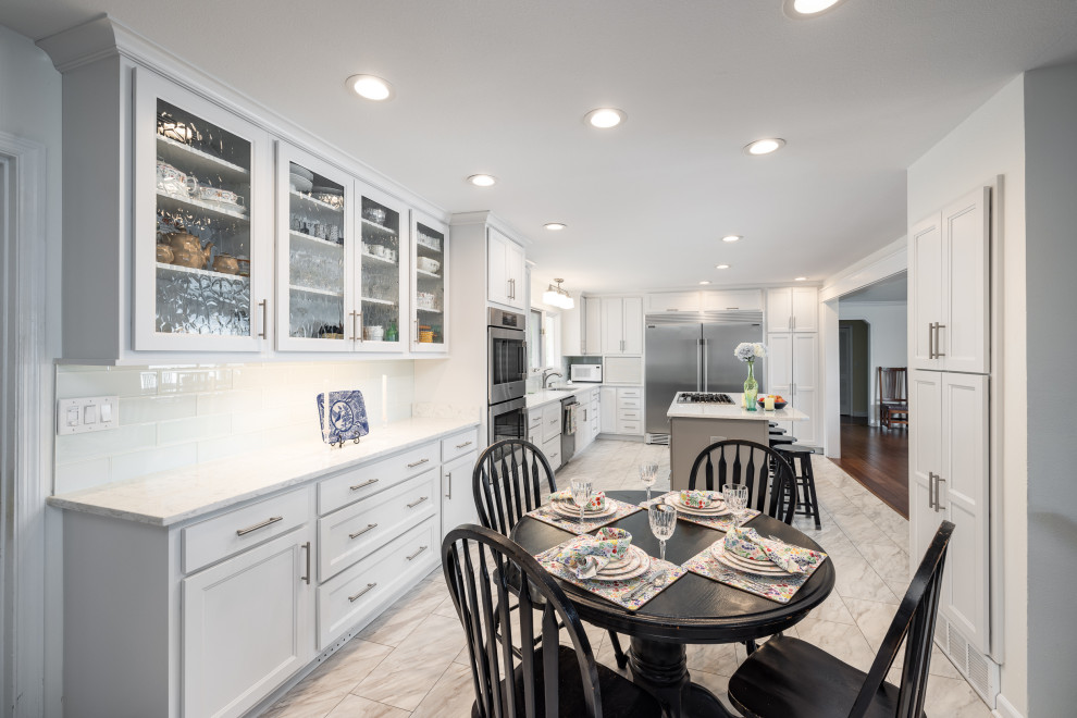 Example of a large transitional l-shaped ceramic tile and white floor enclosed kitchen design with an undermount sink, shaker cabinets, white cabinets, quartz countertops, white backsplash, subway tile backsplash, stainless steel appliances, an island and white countertops
