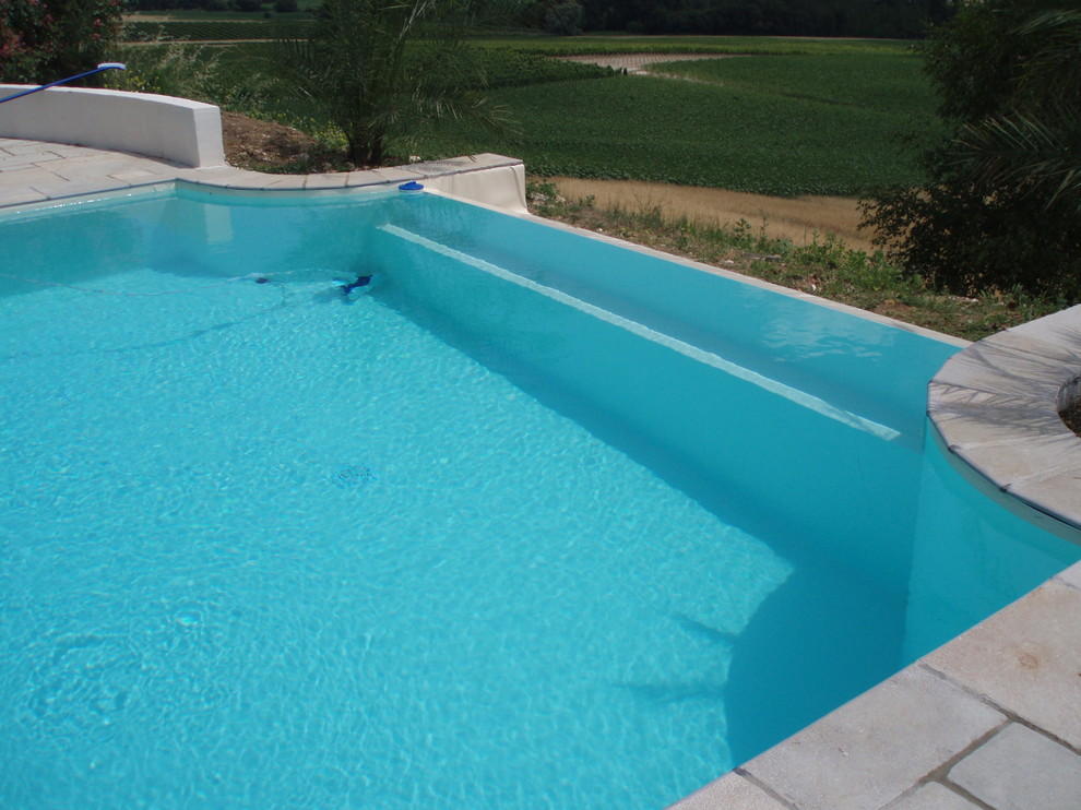 Mid-sized mediterranean rectangular infinity pool in Bordeaux with a water feature and natural stone pavers.