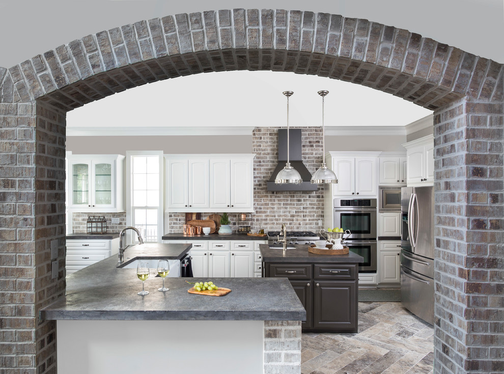 Inspiration for a large transitional u-shaped open plan kitchen in Houston with a farmhouse sink, raised-panel cabinets, white cabinets, concrete benchtops, multi-coloured splashback, brick splashback, stainless steel appliances, travertine floors, multiple islands and multi-coloured floor.