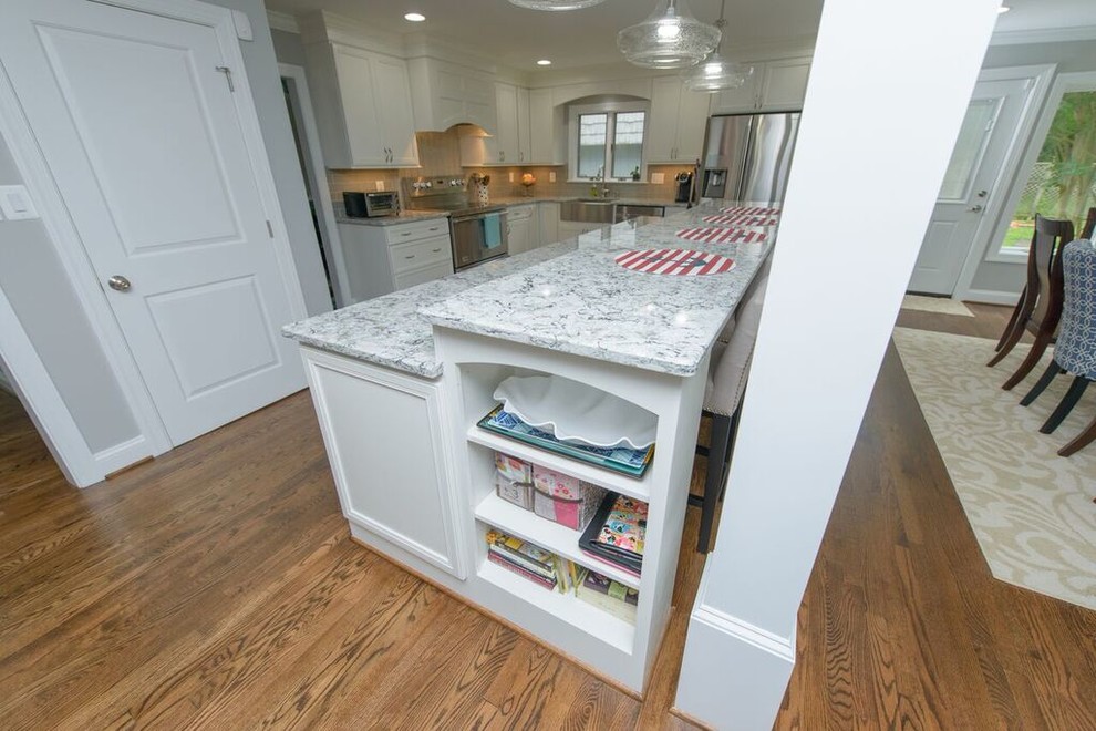 Inspiration for a transitional l-shaped medium tone wood floor eat-in kitchen remodel in Baltimore with a farmhouse sink, beaded inset cabinets, white cabinets, granite countertops, gray backsplash, glass tile backsplash, stainless steel appliances and an island