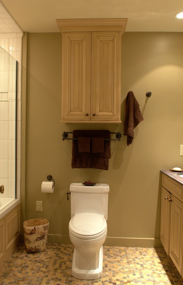 This is an example of a small country bathroom in Burlington with an undermount sink, raised-panel cabinets, light wood cabinets, an alcove tub, a shower/bathtub combo, a two-piece toilet and medium hardwood floors.