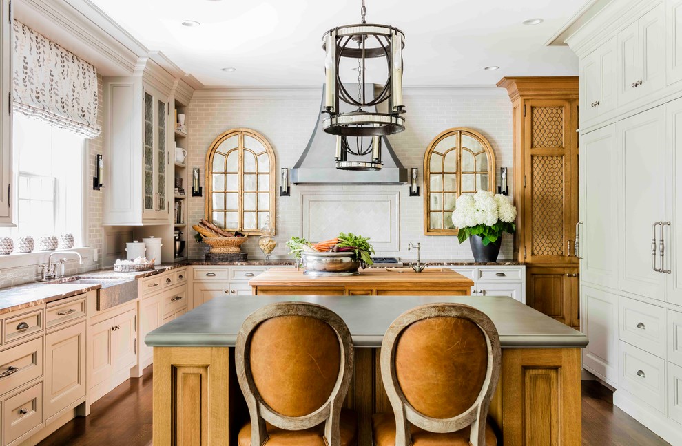 This is an example of a large traditional l-shaped eat-in kitchen in Boston with beaded inset cabinets, medium hardwood floors, multiple islands, white splashback, a farmhouse sink, white cabinets, zinc benchtops, subway tile splashback, stainless steel appliances and brown floor.