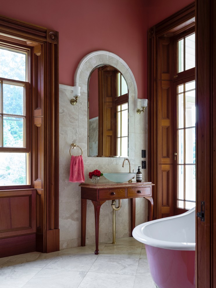 This is an example of a large traditional master bathroom in Wollongong with brown cabinets, a claw-foot tub, beige tile, stone tile, pink walls, marble floors, a vessel sink and marble benchtops.