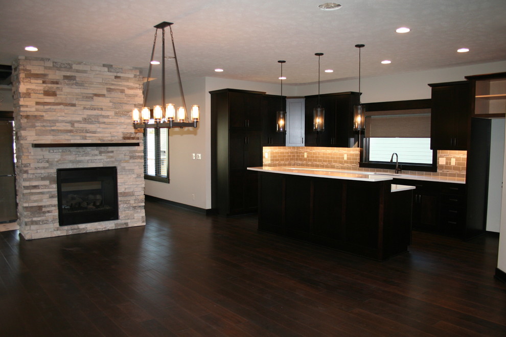 Example of a mid-sized transitional l-shaped dark wood floor and brown floor open concept kitchen design with an undermount sink, shaker cabinets, black cabinets, quartz countertops, beige backsplash, porcelain backsplash, stainless steel appliances and an island