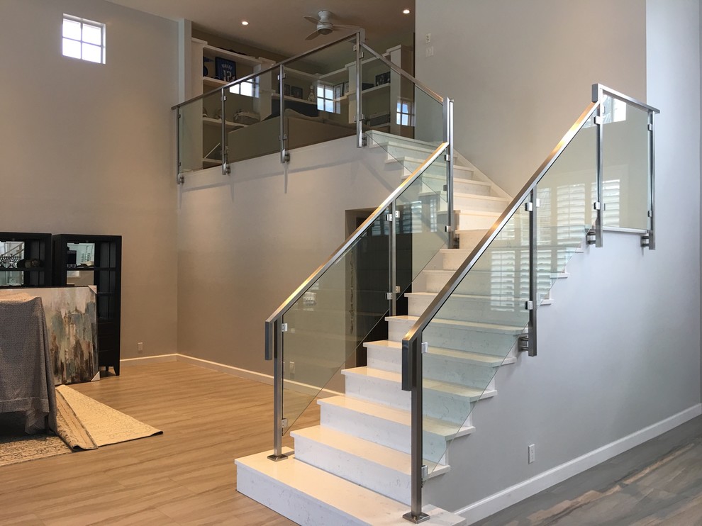 This is an example of a mid-sized modern tile l-shaped staircase in Miami with tile risers and glass railing.