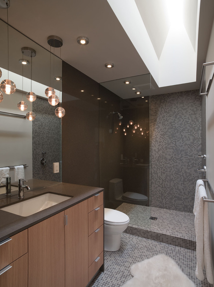 Inspiration for a small contemporary bathroom in Austin with mosaic tile, an open shower, an undermount sink, grey walls, medium wood cabinets, solid surface benchtops, mosaic tile floors, gray tile, an open shower, a one-piece toilet, grey floor, flat-panel cabinets and brown benchtops.