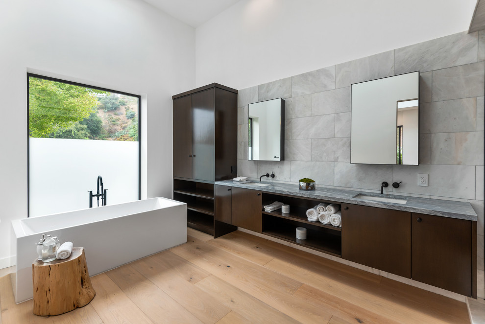 This is an example of a contemporary master bathroom in Los Angeles with flat-panel cabinets, dark wood cabinets, a freestanding tub, gray tile, medium hardwood floors, an undermount sink, engineered quartz benchtops, brown floor, grey benchtops, a double vanity and a floating vanity.