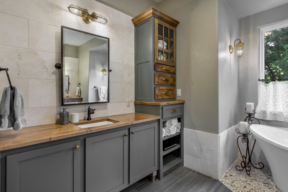 This is an example of a mid-sized traditional master bathroom in Dallas with grey cabinets, a freestanding tub, a curbless shower, a two-piece toilet, white tile, marble, porcelain floors, an undermount sink, wood benchtops, grey floor, a hinged shower door, brown benchtops, a double vanity, a built-in vanity, decorative wall panelling, shaker cabinets and green walls.