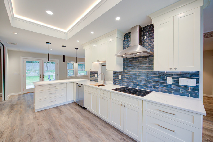This is an example of a mid-sized transitional galley eat-in kitchen in New York with an undermount sink, shaker cabinets, white cabinets, solid surface benchtops, blue splashback, subway tile splashback, stainless steel appliances, medium hardwood floors, a peninsula, beige floor and white benchtop.