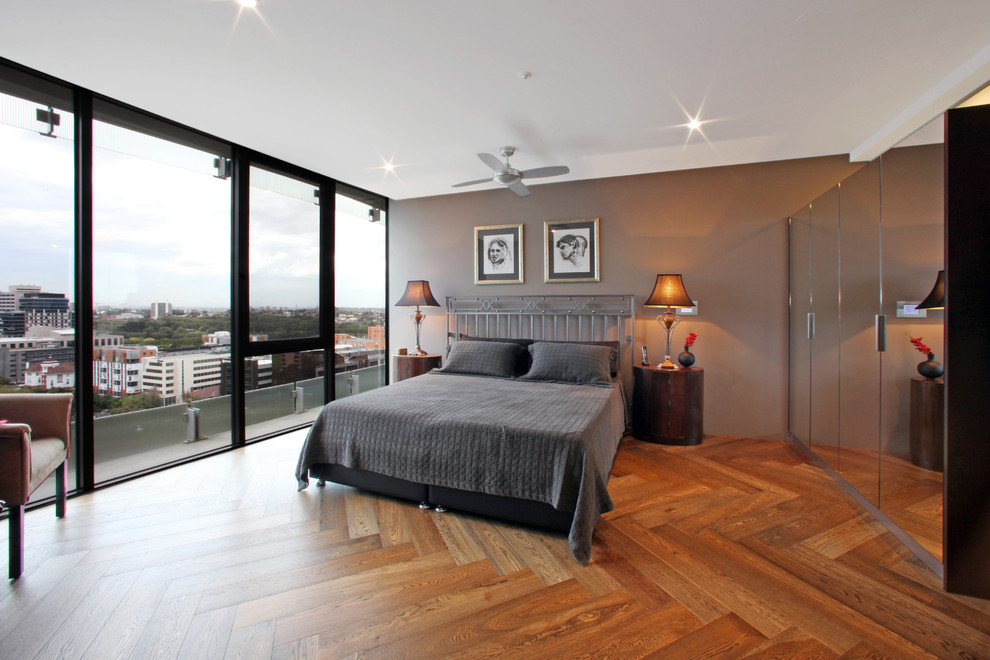 Modern bedroom in Melbourne with brown walls, medium hardwood floors and no fireplace.