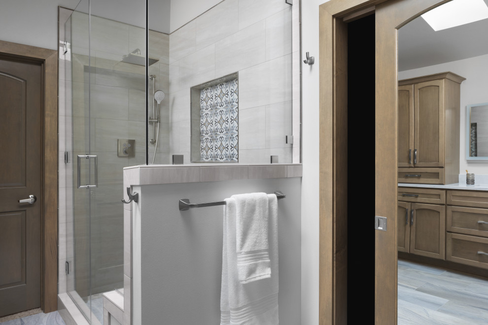 Photo of a mid-sized transitional master bathroom in Milwaukee with recessed-panel cabinets, medium wood cabinets, a drop-in tub, an alcove shower, a two-piece toilet, porcelain tile, beige walls, porcelain floors, an undermount sink, engineered quartz benchtops, blue floor, a hinged shower door, white benchtops, a niche, a double vanity and a built-in vanity.