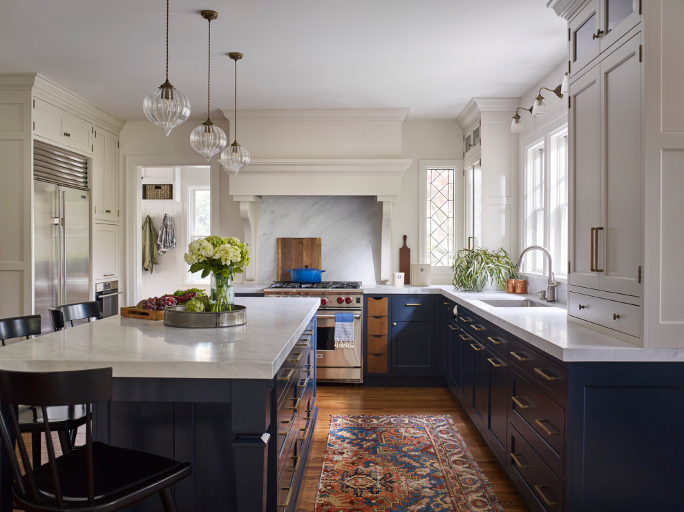 Photo of a large traditional u-shaped eat-in kitchen in New York with a farmhouse sink, shaker cabinets, blue cabinets, marble benchtops, white splashback, marble splashback, stainless steel appliances, medium hardwood floors, with island, brown floor and white benchtop.