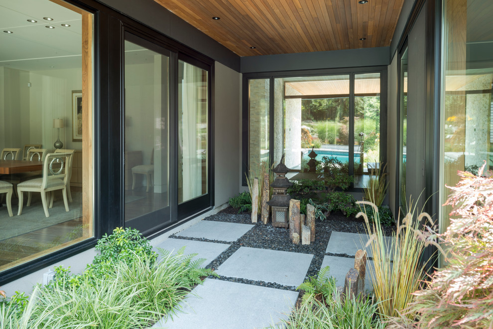 This is an example of a contemporary courtyard patio in Vancouver with a roof extension.