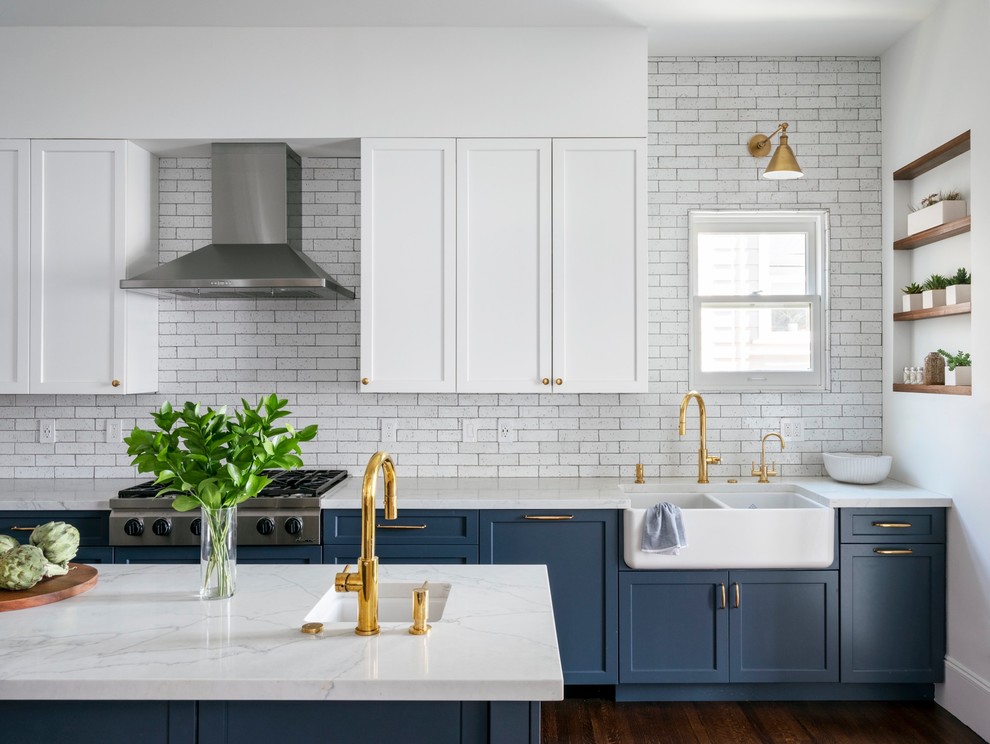 This is an example of a transitional kitchen in San Francisco with a farmhouse sink, quartz benchtops, white splashback, stainless steel appliances, with island, brown floor, white benchtop, shaker cabinets, blue cabinets, subway tile splashback and dark hardwood floors.