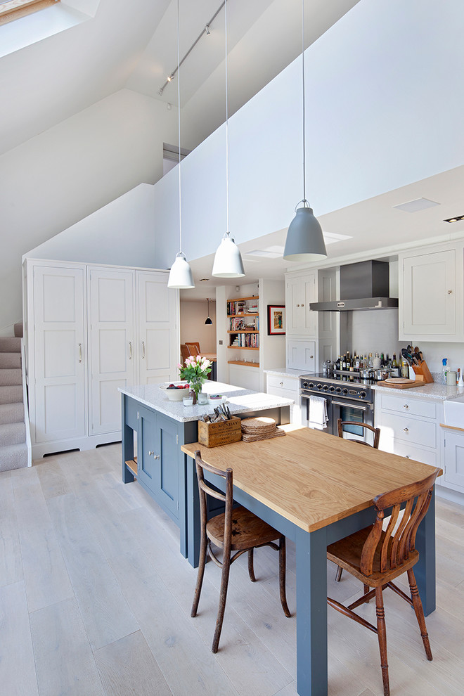 Scandinavian single-wall eat-in kitchen in Oxfordshire with a farmhouse sink, shaker cabinets, white cabinets, stainless steel appliances, light hardwood floors and with island.