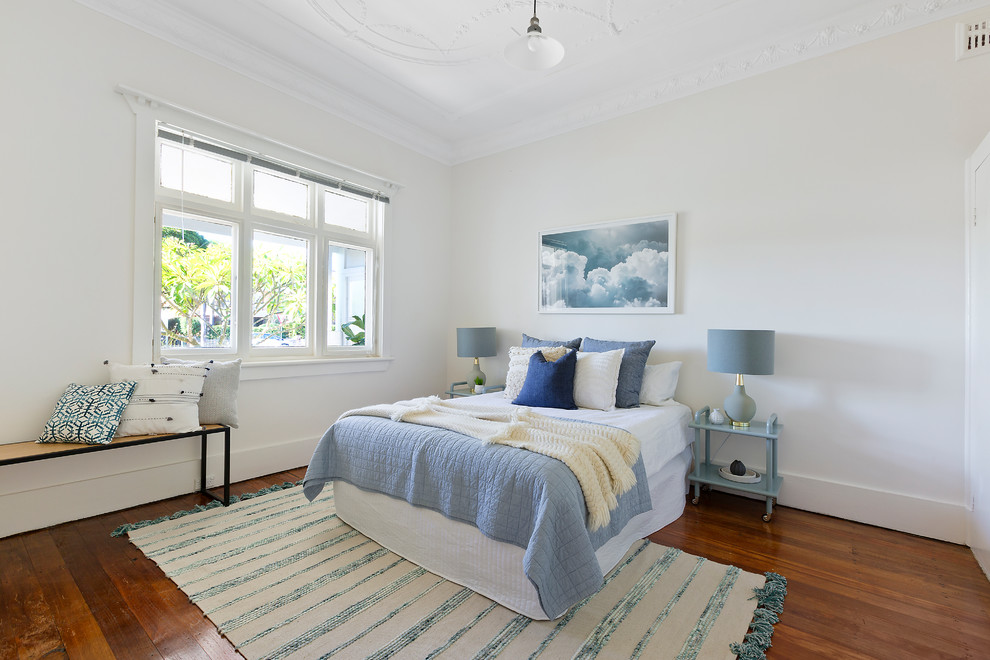 Photo of a beach style guest bedroom in Sydney with white walls, dark hardwood floors and brown floor.