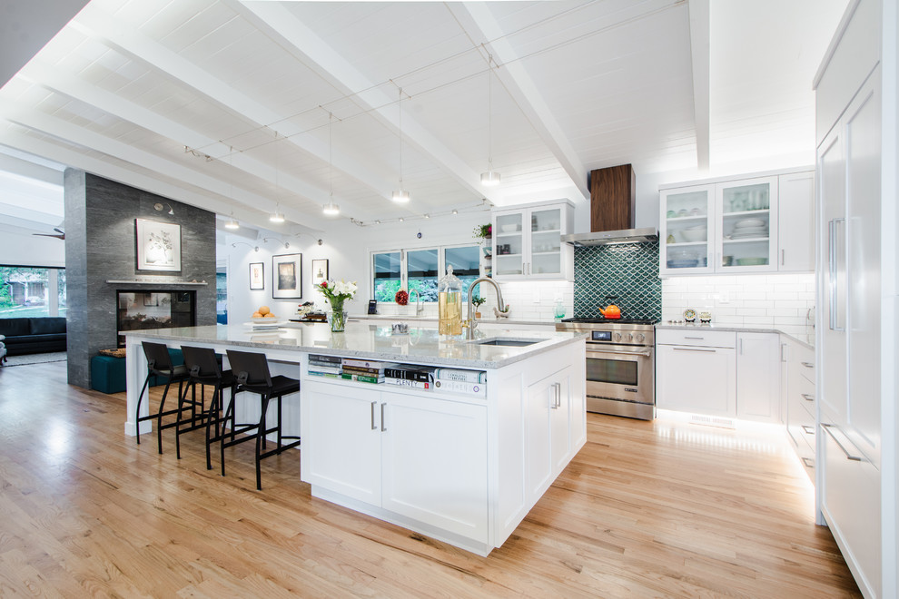 Photo of a large midcentury l-shaped eat-in kitchen in Denver with shaker cabinets, an undermount sink, white cabinets, granite benchtops, green splashback, mosaic tile splashback, panelled appliances, light hardwood floors, with island and grey benchtop.