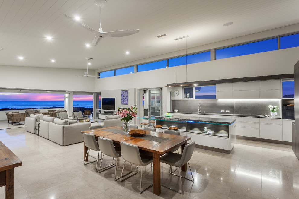 This is an example of a large beach style open concept living room in Perth with white walls, travertine floors, a standard fireplace, a plaster fireplace surround, a wall-mounted tv and beige floor.
