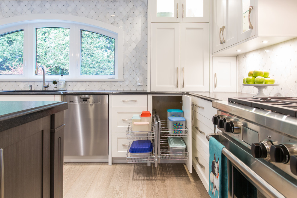 Example of a large transitional l-shaped medium tone wood floor and beige floor eat-in kitchen design in Vancouver with an undermount sink, shaker cabinets, white cabinets, granite countertops, gray backsplash, marble backsplash, stainless steel appliances, an island and black countertops