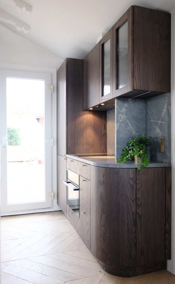 This is an example of a small contemporary galley open plan kitchen in Other with an undermount sink, glass-front cabinets, dark wood cabinets, granite benchtops, grey splashback, granite splashback, panelled appliances, light hardwood floors, grey benchtop and exposed beam.