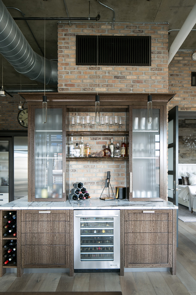 This is an example of a mid-sized industrial single-wall wet bar in Denver with no sink, recessed-panel cabinets, dark wood cabinets, marble benchtops, multi-coloured splashback, brick splashback, medium hardwood floors and grey floor.