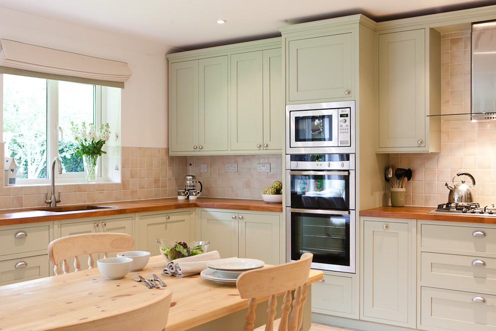 Inspiration for a traditional eat-in kitchen in Berkshire with wood benchtops, green cabinets, shaker cabinets, beige splashback and stainless steel appliances.