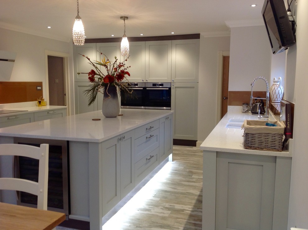 Large contemporary galley eat-in kitchen in Cambridgeshire with a double-bowl sink, shaker cabinets, grey cabinets, quartzite benchtops, metallic splashback, mirror splashback, stainless steel appliances, medium hardwood floors and with island.