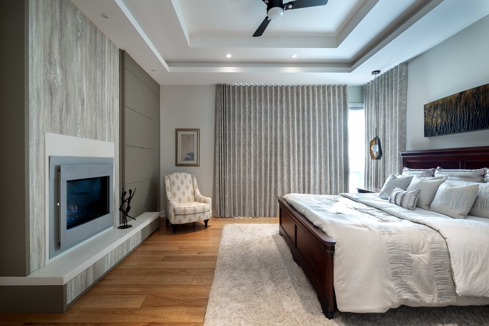 This is an example of a large contemporary master bedroom in Ottawa with grey walls, medium hardwood floors, a two-sided fireplace, a plaster fireplace surround and brown floor.