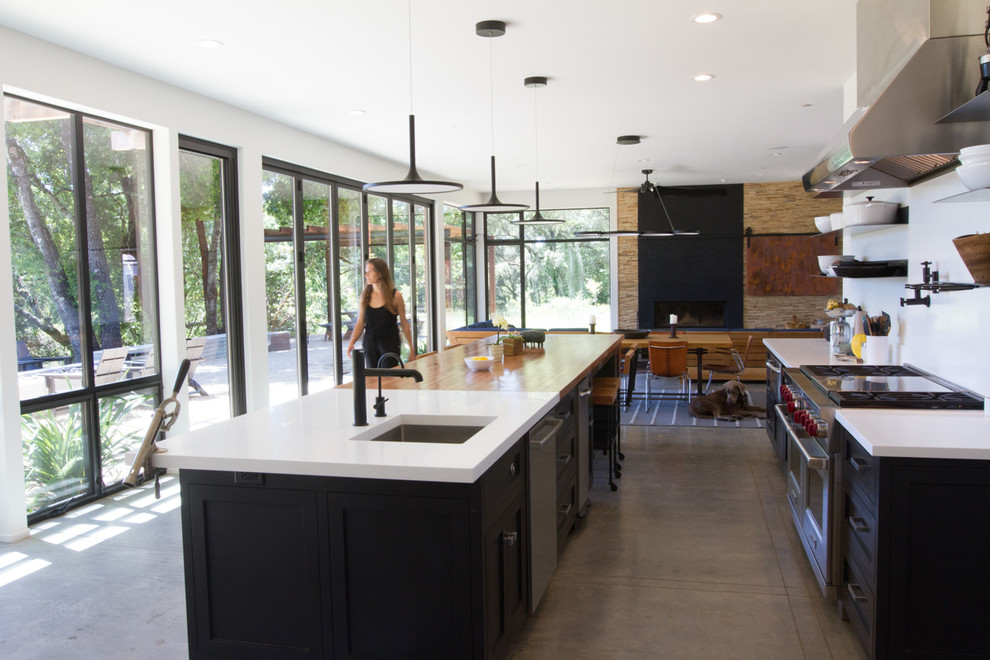 Design ideas for a country galley open plan kitchen in San Francisco with black cabinets, wood benchtops, white splashback, stainless steel appliances, concrete floors, with island, grey floor, white benchtop, an undermount sink and shaker cabinets.