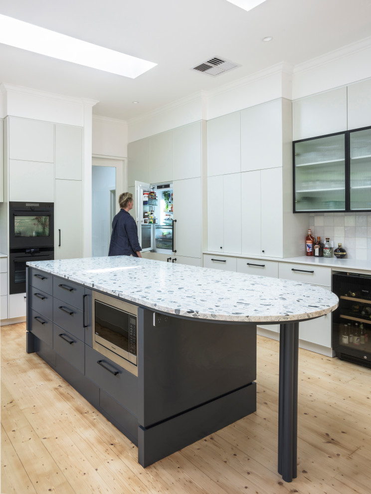 This is an example of a large contemporary u-shaped open plan kitchen in Melbourne with a double-bowl sink, beige cabinets, terrazzo worktops, black appliances, light hardwood flooring and multicoloured worktops.