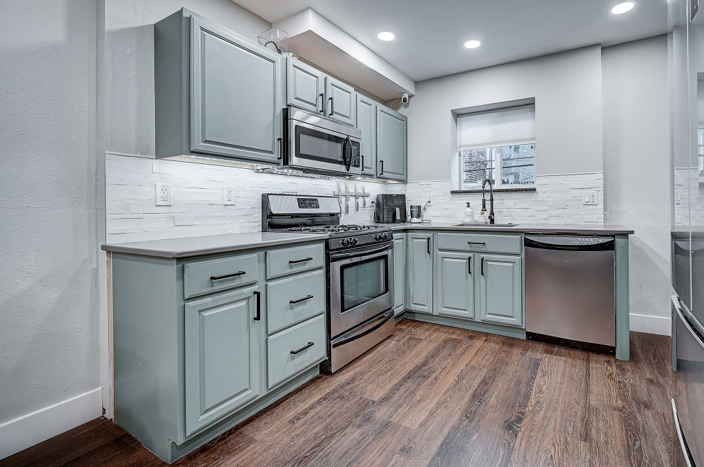 Foto på ett litet minimalistiskt grå kök, med en nedsänkt diskho, luckor med profilerade fronter, gröna skåp, bänkskiva i rostfritt stål, vitt stänkskydd, stänkskydd i kalk, rostfria vitvaror, vinylgolv, flera köksöar och brunt golv