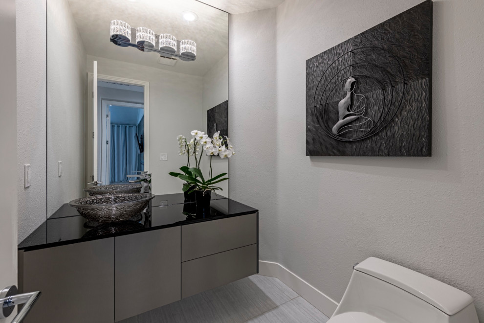 Пример оригинального дизайна: туалет среднего размера в стиле модернизм с серыми фасадами, серыми стенами, стеклянной столешницей, серым полом, черной столешницей и подвесной тумбой