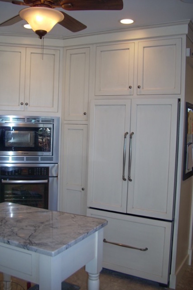 Eat-in kitchen - large transitional l-shaped travertine floor and beige floor eat-in kitchen idea in Boston with a farmhouse sink, recessed-panel cabinets, white cabinets, granite countertops, white backsplash, subway tile backsplash, paneled appliances, an island and black countertops
