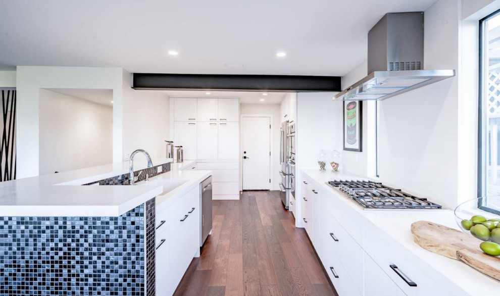 This is an example of a small contemporary galley eat-in kitchen in Orange County with an undermount sink, flat-panel cabinets, white cabinets, quartz benchtops, white splashback, stainless steel appliances, medium hardwood floors, with island, brown floor and white benchtop.