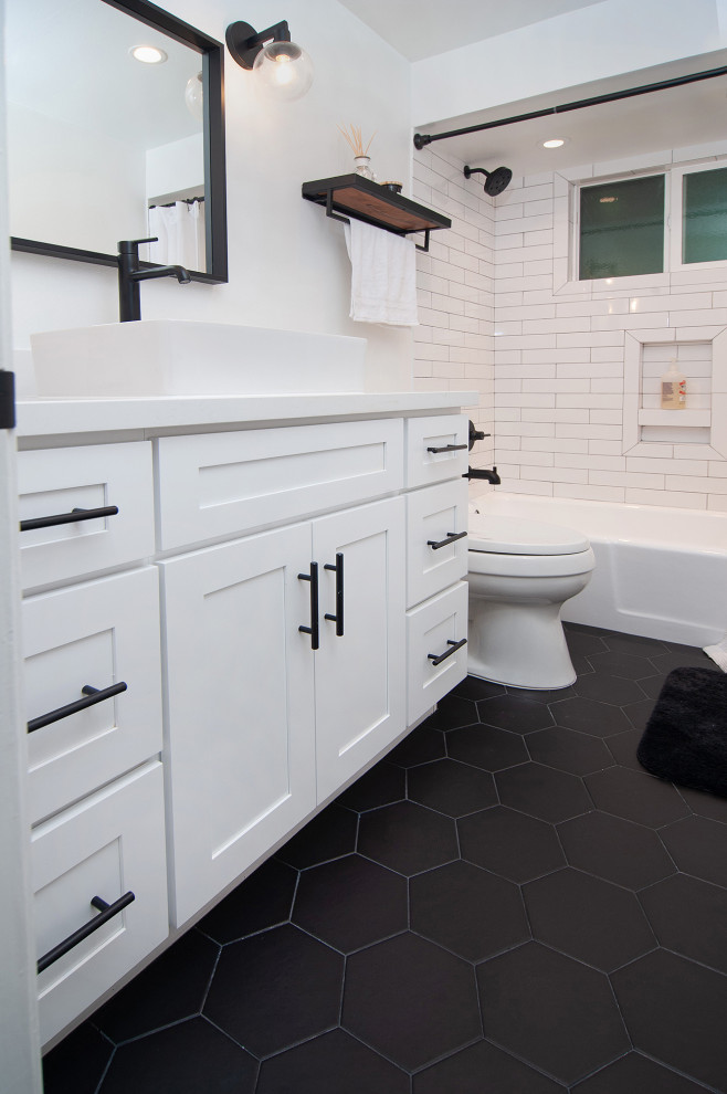 Photo of a mid-sized industrial 3/4 bathroom in San Diego with shaker cabinets, white cabinets, an alcove tub, a two-piece toilet, white tile, subway tile, white walls, porcelain floors, white benchtops, a shower/bathtub combo, a vessel sink, black floor and a shower curtain.