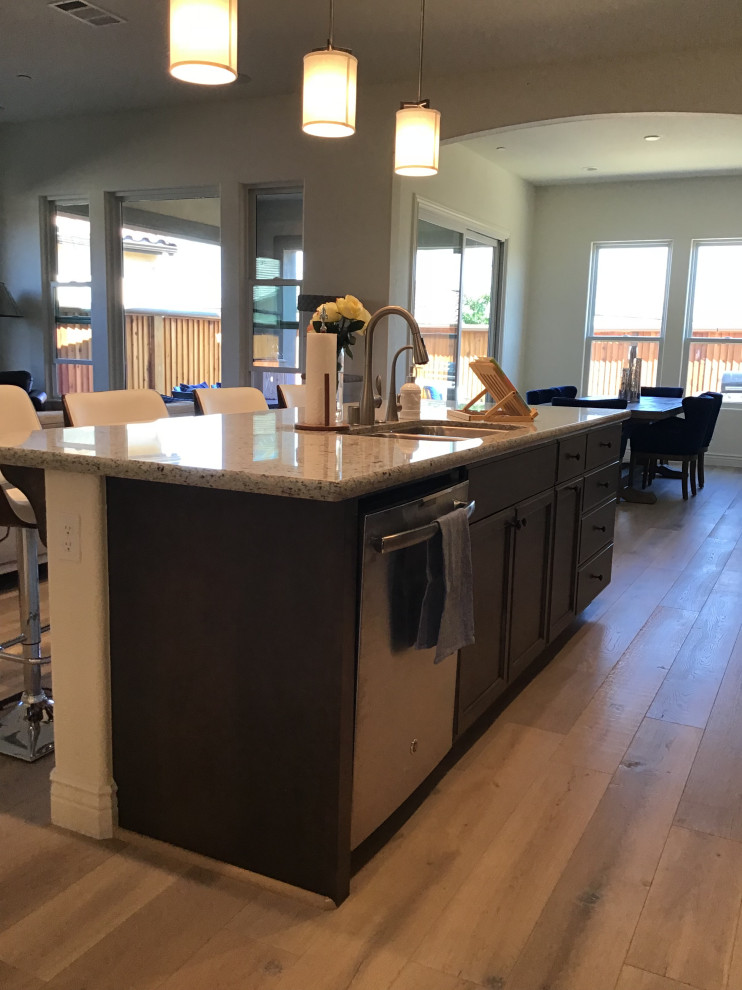 Large traditional galley eat-in kitchen in Other with dark wood cabinets, granite benchtops, stainless steel appliances, light hardwood floors, with island, multi-coloured benchtop, a drop-in sink, recessed-panel cabinets and recessed.