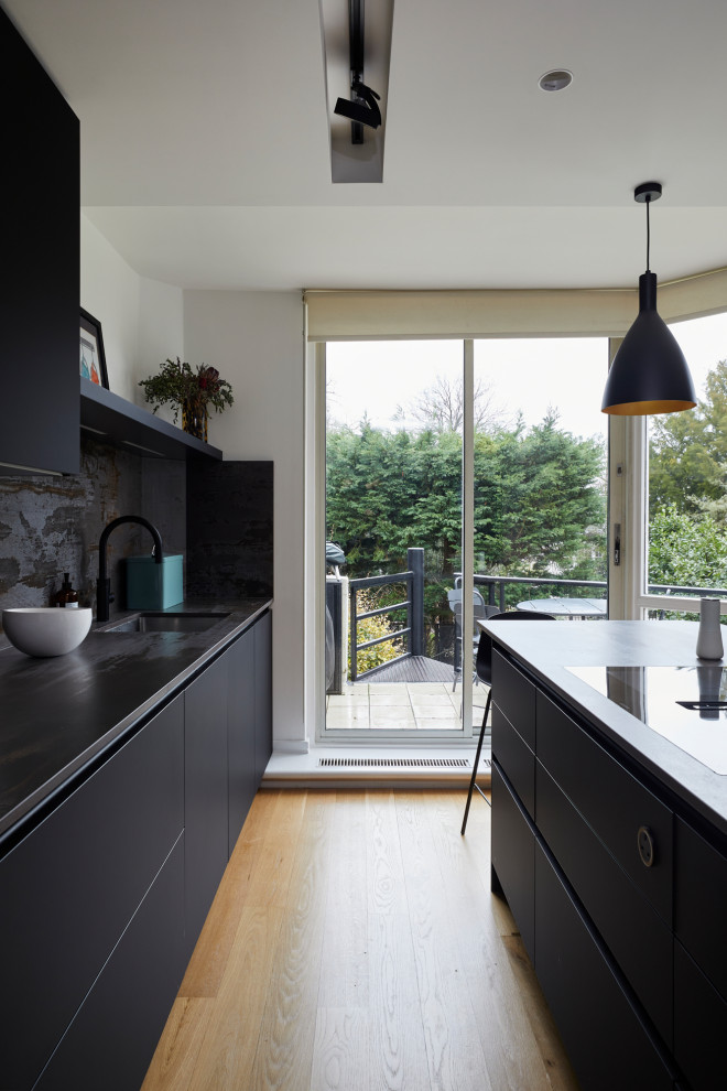 Design ideas for a small modern l-shaped separate kitchen in London with an undermount sink, flat-panel cabinets, quartz benchtops, multi-coloured splashback, engineered quartz splashback, black appliances, light hardwood floors, with island and multi-coloured benchtop.